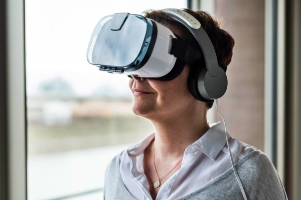 Woman standing next to a window wearing virtual reality glasses and headphones.